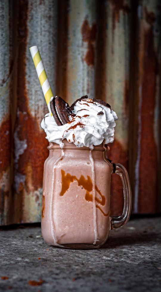 Glass with a handle filled with chocolate milkshake, topped with whipped cream and oreos. Finished off with a straw