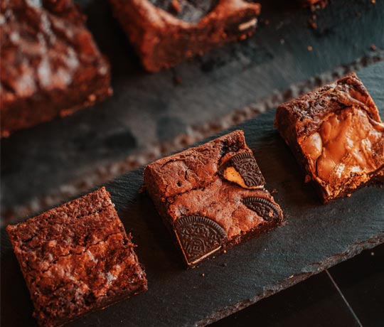 Looking down on squares of different flavoured brownies on a wooden surface,