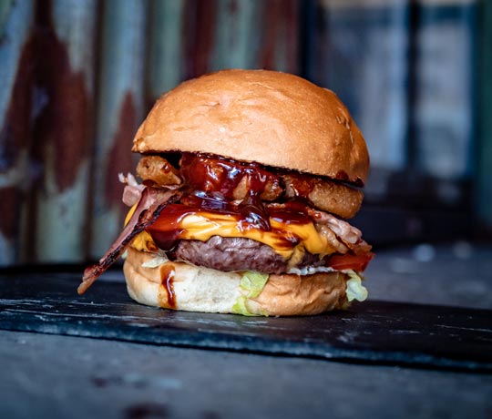 Beef burger in a brioche bun filled with bacon, onion rings, cheese and oozing with BBQ sauce