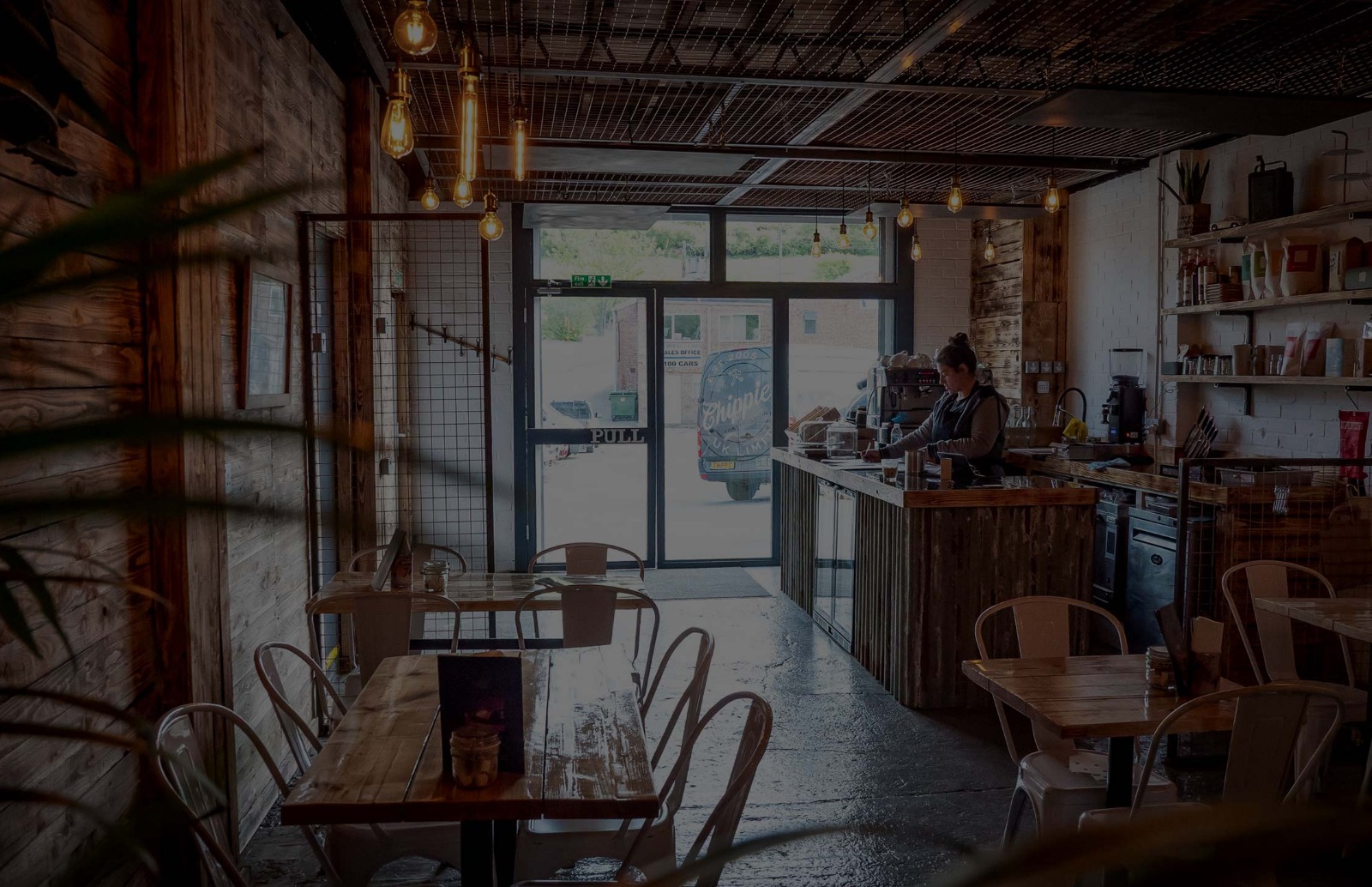 Fuel Burgers Coffee Shop located for collection and delivery in Small Dole View of a coffee shop with an out of focus plant, tables with menus on and a counter with a lady making coffee behind.